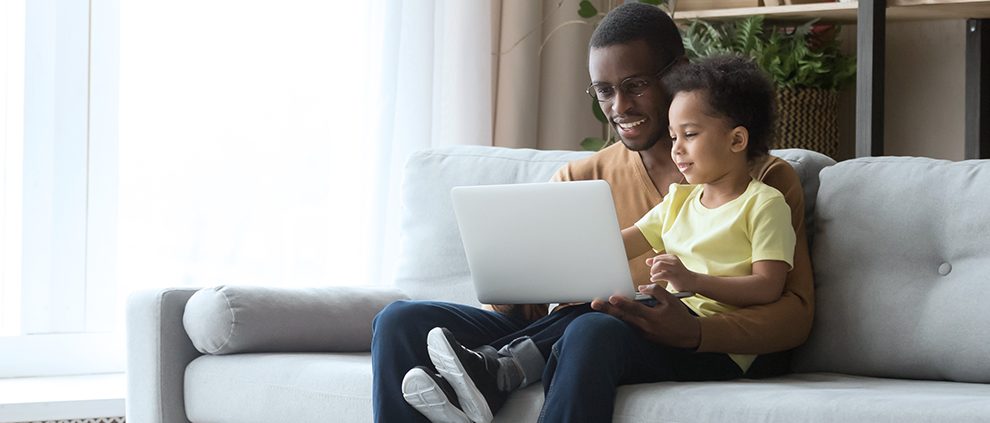 man sitting on the couch with a child and laptop